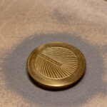 Bronze medallion with YANNIS SERGAKIS engraving and sunburst pattern - commemorative design piece displayed at Queeng Studio